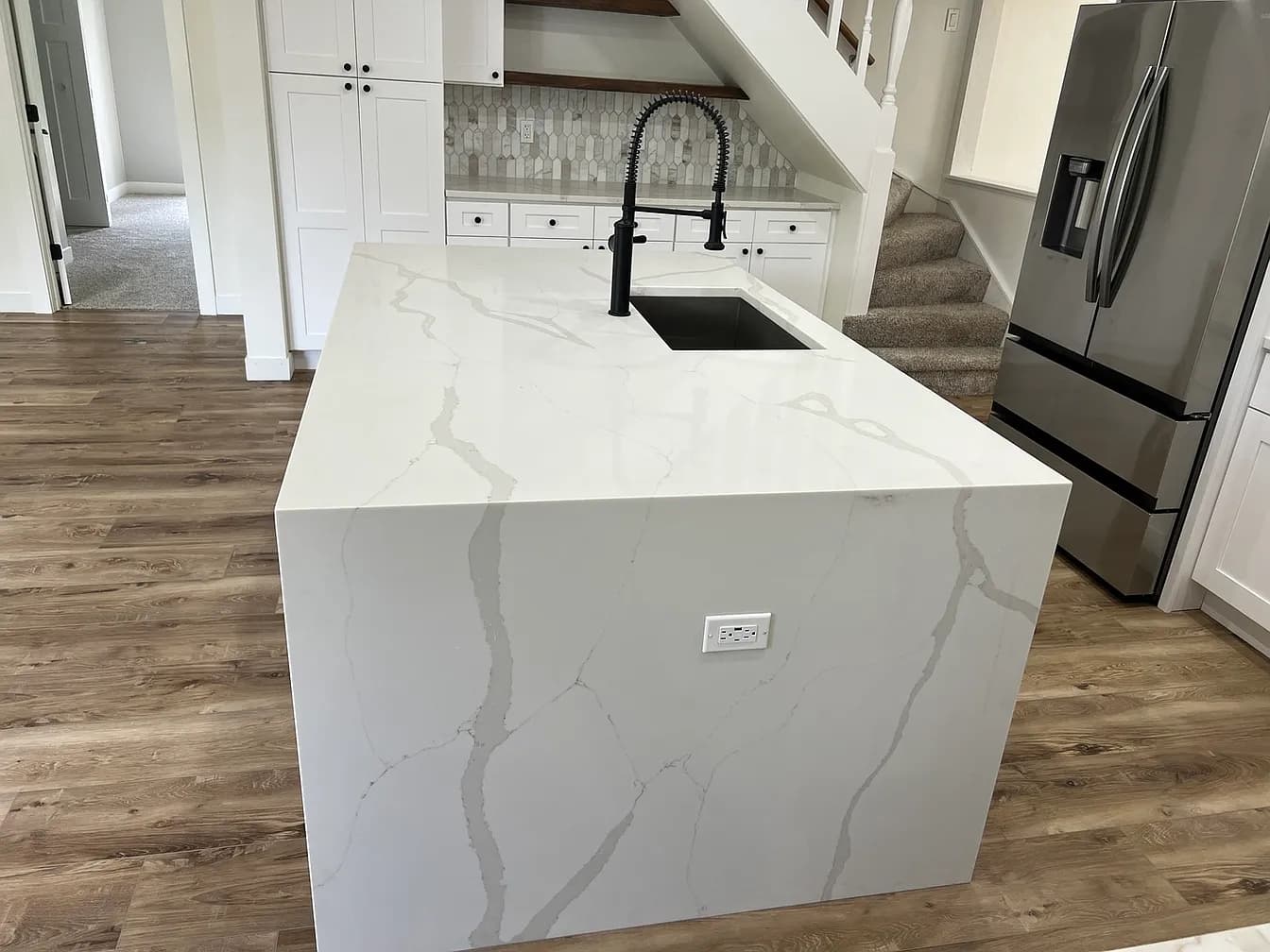 Close-up of the quartz waterfall island, black pull-down faucet, and deep undermount sink in the Libertyville kitchen remodel