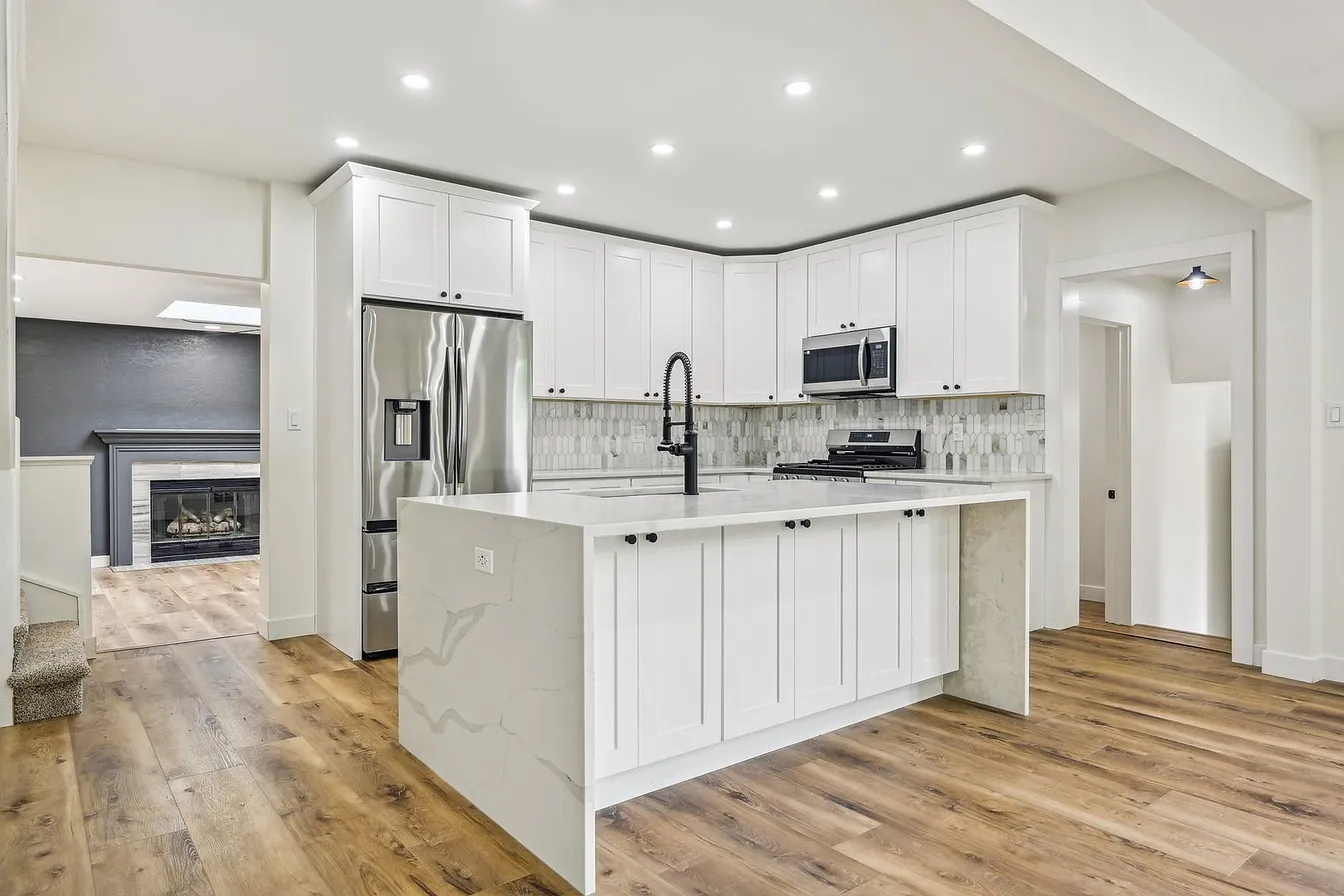 Finished open-concept kitchen remodel in Libertyville, IL with white shaker cabinets, a quartz waterfall island, and stainless appliances, open to the living room